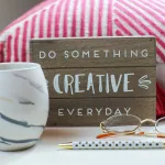 Stylish desk setup with a coffee mug, eyeglasses, and motivating sign.